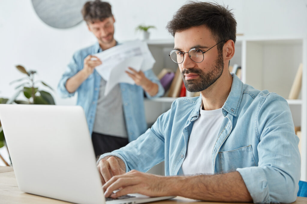 bearded man freelancer works laptop computer keyboards information thinks about profits